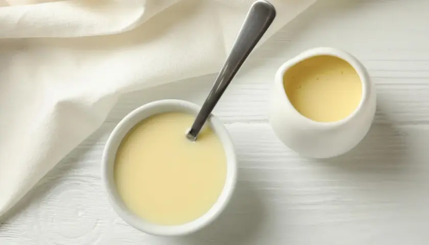 Crema amarilla en un cuenco con cuchara y jarrita, ideal para sustituir nata para cocinar por leche en recetas ligeras.