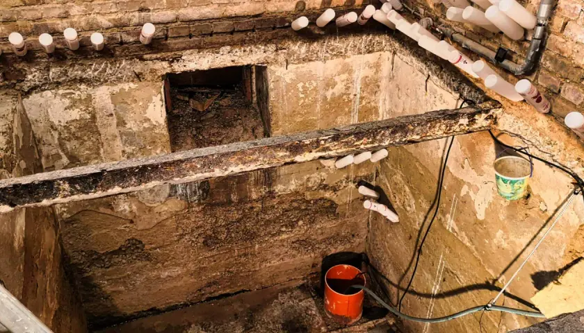 Feuchter Keller mit aufstauendem Sickerwasser, Rohren und einem Eimer zur Entwässerung.