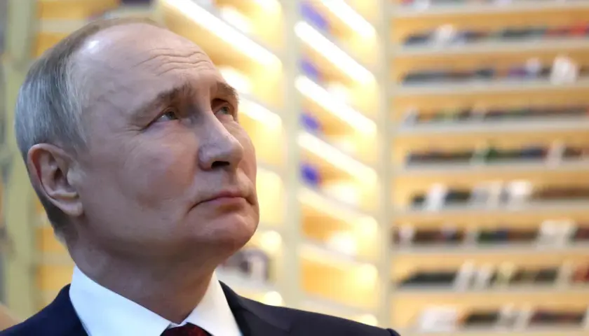 Nahaufnahme von Wladimir Putin, der nachdenklich in die Ferne blickt. Die Hintergrundbeleuchtung deutet auf eine Veranstaltung hin, vielleicht im Zusammenhang mit den Russland Wahlen.