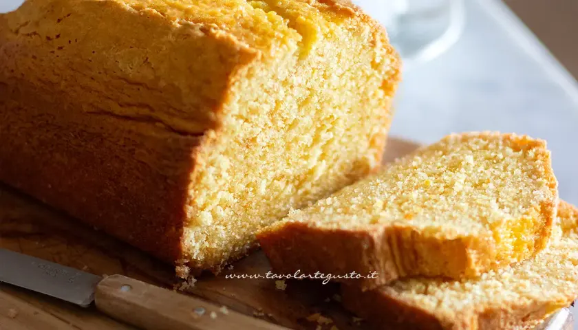 Plumcake senza yogurt dorato e soffice, tagliato a fette su un tagliere di legno con un coltello.