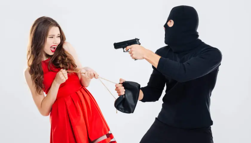 Una mujer con vestido rojo grita mientras un ladrón enmascarado le apunta con una pistola y tira de su bolso. Es como soñar que te roban.
