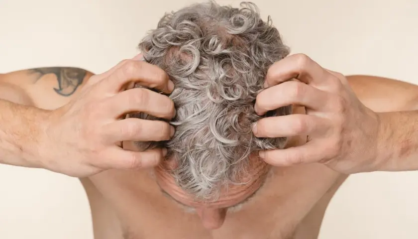 Hombre rascándose el cuero cabelludo con pelo gris y rizado.