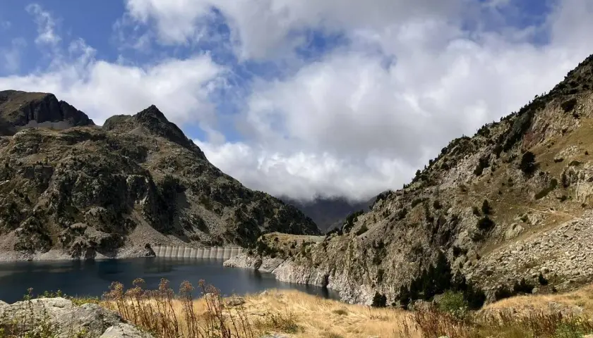Paisaje montañoso con un embalse azul, ideal para rutas en Sallent de Gállego. Nubes y vegetación agreste completan la escena.