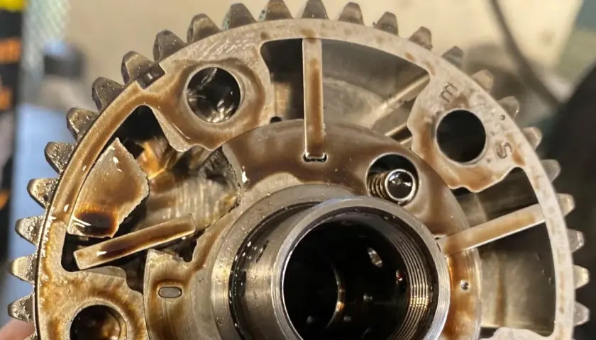 Widok z bliska na koła zmiennych faz rozrządu, z widocznymi elementami mechanicznymi i śladami oleju.
