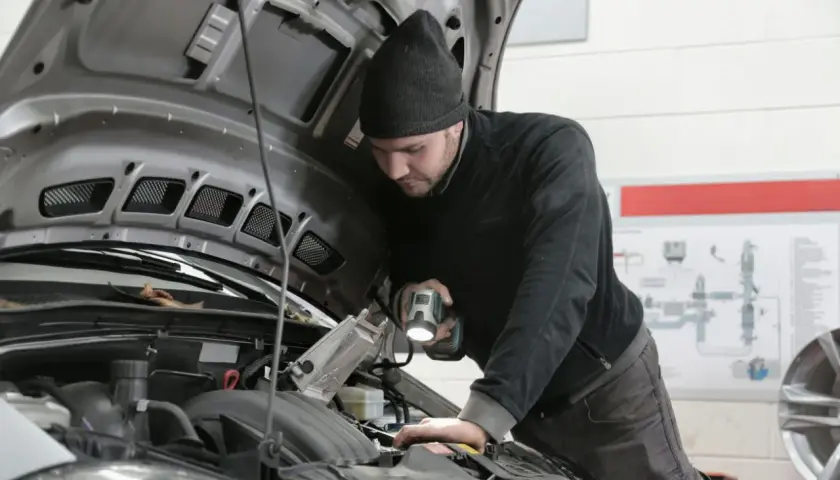 Mechanik z latarką bada silnik Renault, szukając przyczyny błędu DTC P0380.