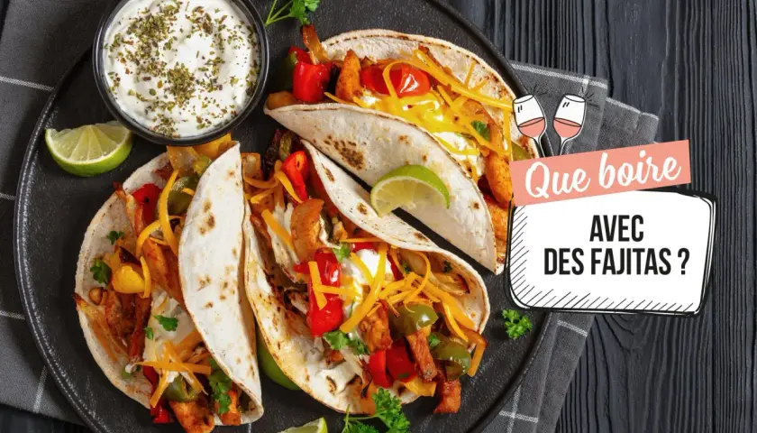 Assiette de fajitas savoureuses avec garnitures, crème aigre et quartiers de citron vert. Le texte demande "Que boire avec des fajitas ?".