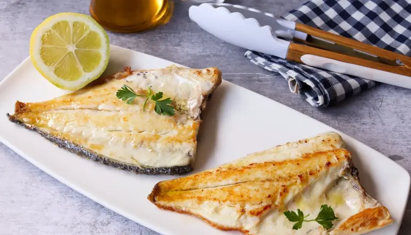 Dos filetes de dorada a la plancha, jugosos y dorados, servidos con perejil fresco y una rodaja de limón.