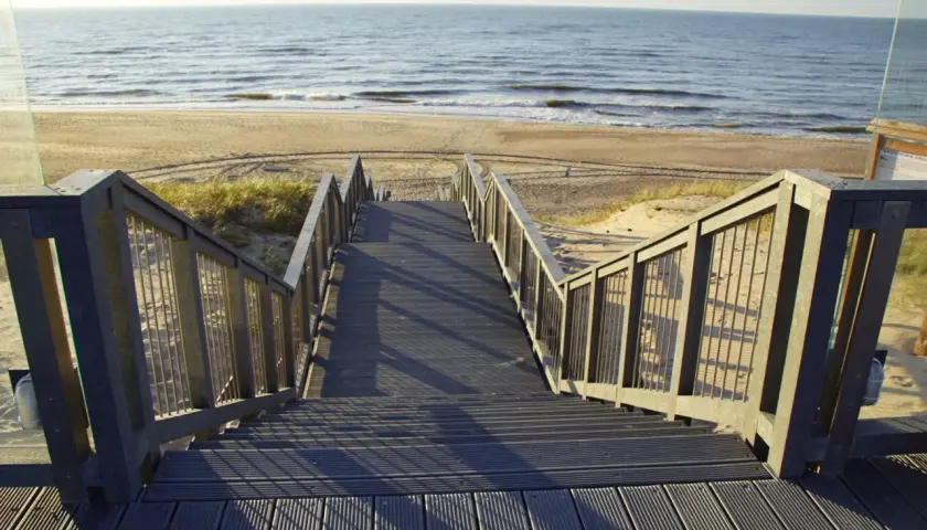 Schody prowadzące na plażę w Darłówku. Promenada z widokiem na morze i piasek.