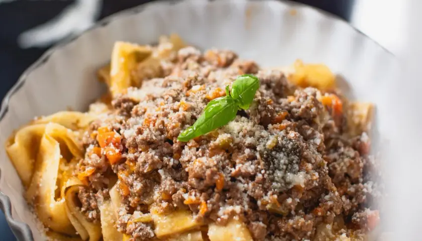 Un plat de pâtes fraîches, garni d'une sauce bolognaise riche et savoureuse, parsemé de parmesan et d'une feuille de basilic. Une recette spaghetti bolognaise italienne authentique.