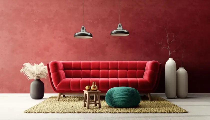 Soggiorno moderno con divano rosso vellutato e **effetto spugnato muro** color bordeaux. Due lampade a sospensione, pouf verde acqua e vasi bianchi completano l'arredo.