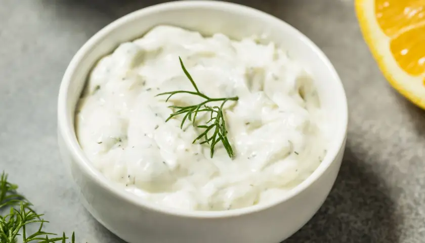 Salsa yogurt ricetta cremosa con aneto fresco e una fetta di limone sullo sfondo.