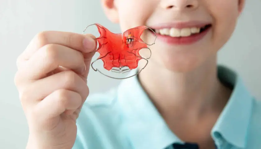 Niño sonriente muestra un aparato de ortodoncia rojo, un twin block, para corregir su mordida.