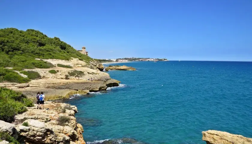 Dos personas caminan por el camí de ronda en Tarragona, disfrutando de las vistas al mar Mediterráneo y la costa.