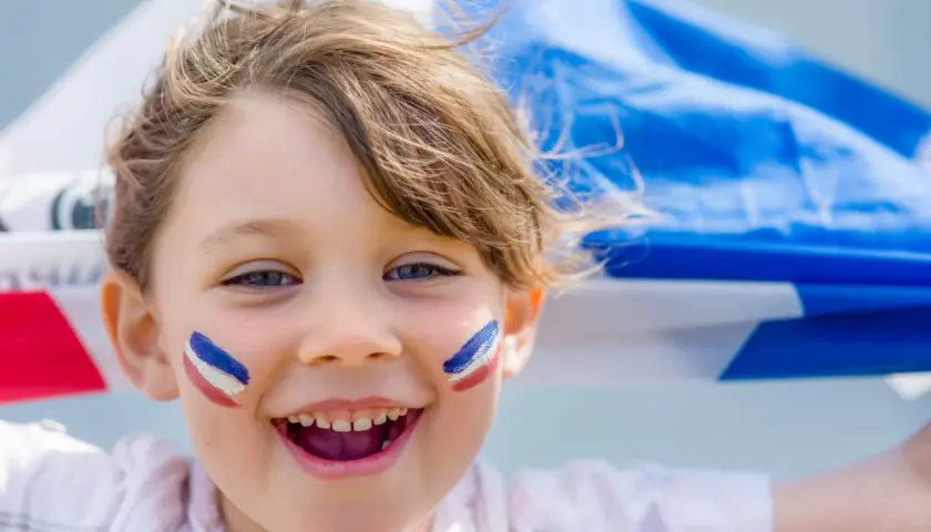 Uśmiechnięta Agnieszka z francuskimi barwami na policzkach, trzymająca flagę Francji.