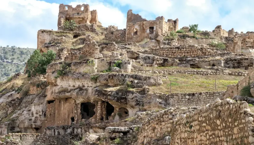 Ruiny starożytnego miasta Hasankeyf na skalistym zboczu, z widocznymi jaskiniami i kamiennymi murami.