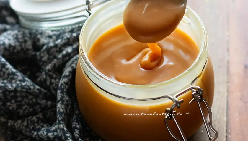Caramello salato ricetta: un cucchiaio raccoglie la salsa dorata da un barattolo di vetro.
