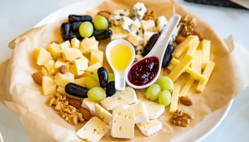 Un tagliere ricco di formaggio semistagionato, uva, noci, mandorle, miele e marmellata.