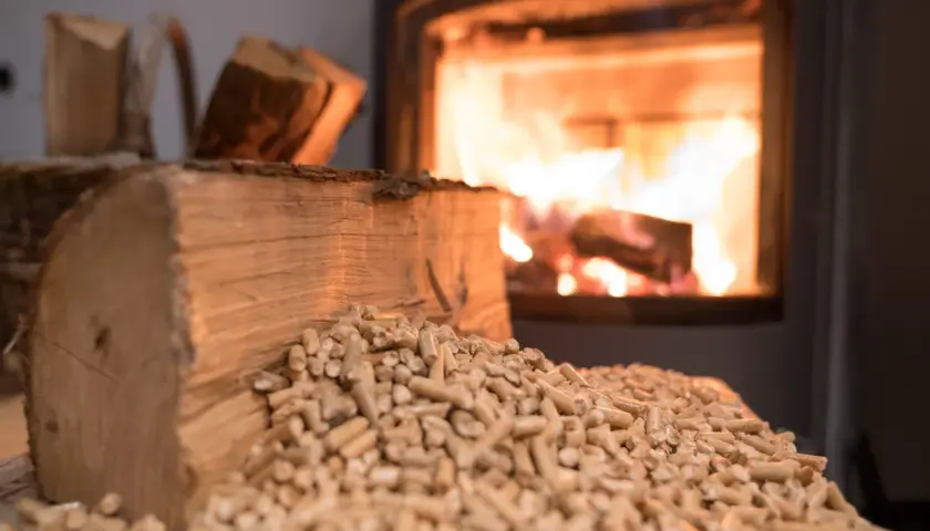 Holzscheite und Pellets liegen bereit, während im Kamin das Feuer lodert. Bauholz im Kamin verbrennen sorgt für wohlige Wärme.