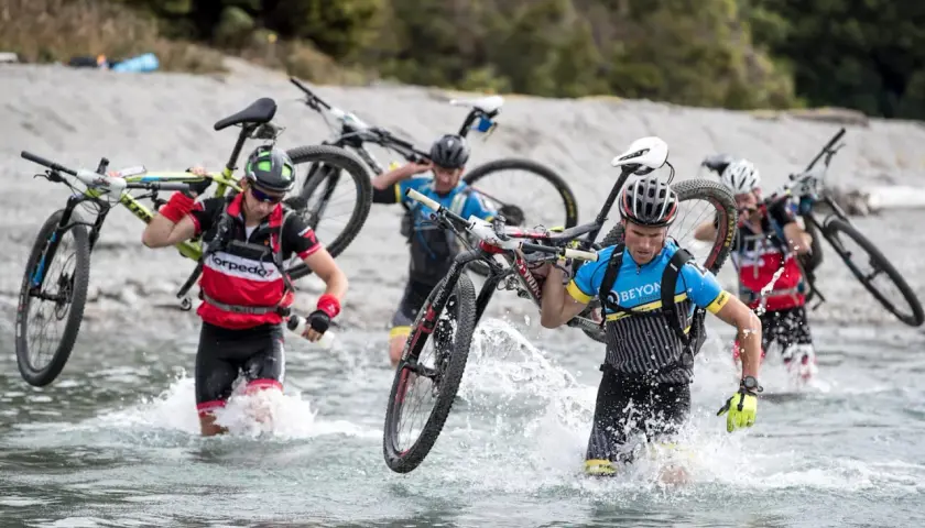 Teilnehmer eines **adventure racing** durchqueren mit ihren Mountainbikes einen Fluss.