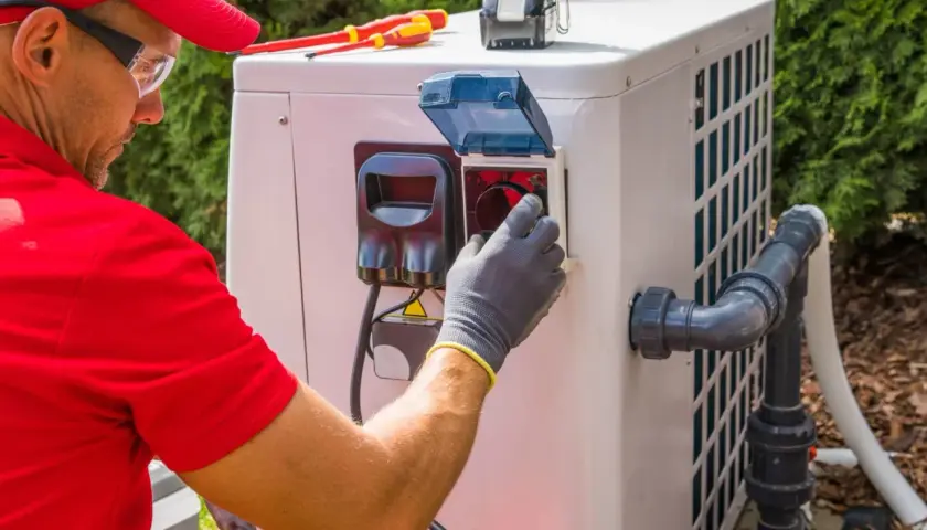 Technik w rękawiczkach sprawdza panel pompy ciepła, by zapewnić optymalną, jaką temperaturę daje pompa ciepła. Narzędzia leżą obok.