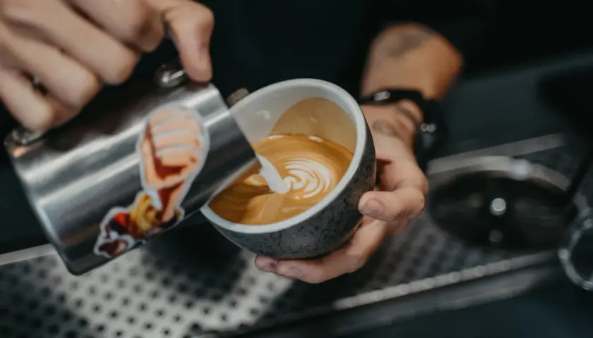 Barista tworzy wzorek na kawie, nalewając spienione mleko. To prosty sposób, jak zrobić wzorek na kawie.