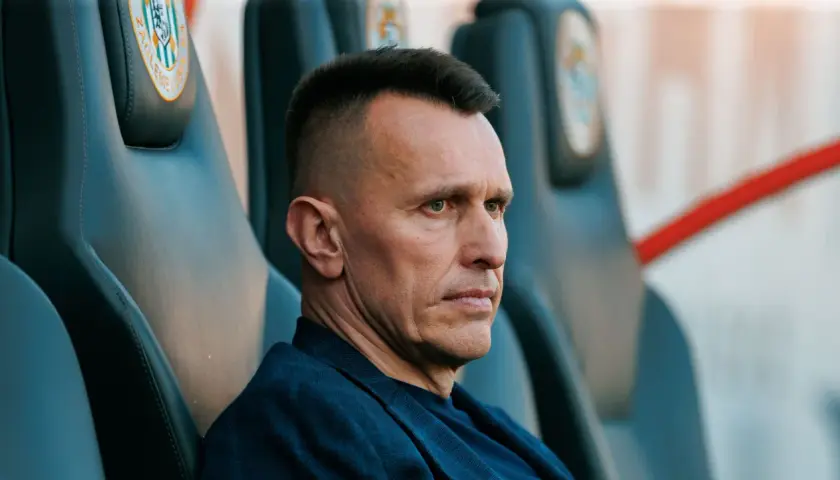 Skupiony trener Zagłębia Lubin siedzi na ławce rezerwowych, analizując grę.