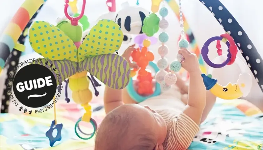 En bebis leker under en färgglad babygym med en söt kanin som hänger.