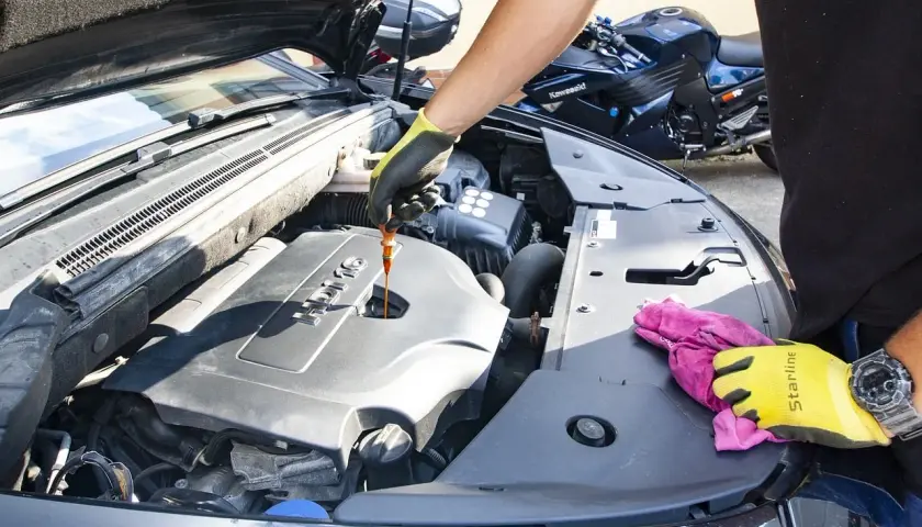Persona con guantes revisa el nivel de aceite del motor, un paso clave para saber como cambiar el aceite del coche.