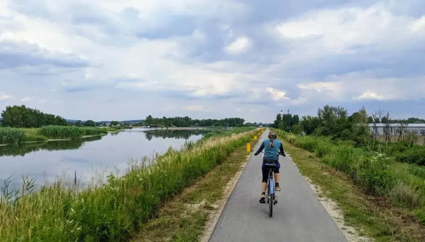 Kobieta na rowerze przemierza ścieżkę nad wodą, ciesząc się pięknem przyrody. To idealne miejsce na **velo Skawina**.