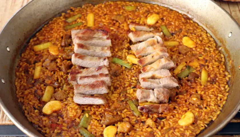 Arroz con secreto de cerdo, jugoso y dorado, con trozos de carne y verduras en una paellera.