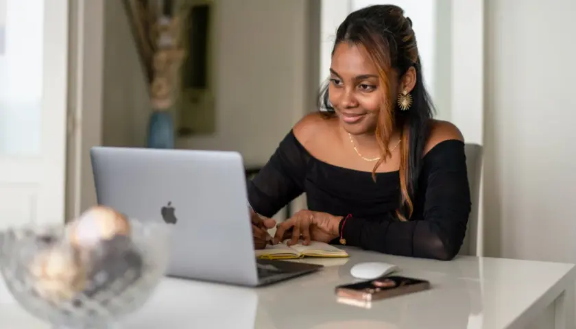 Giovane donna sorride mentre studia o lavora al computer, forse per insegnare inglese online.