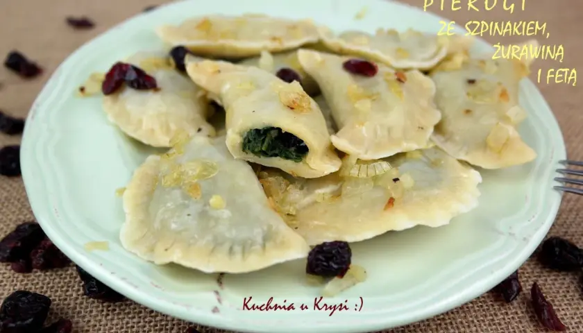 Pyszne pierogi ze szpinakiem i serem feta, okraszone cebulką i żurawiną, na talerzu.