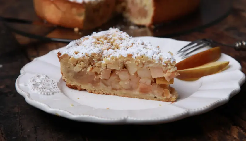 Ein Stück Apfelkuchen mit Streuseln und Puderzucker, perfekt für ein gemütliches apfelkuchen rezept.