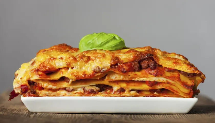 Una porción generosa de lasagna italiana, con capas de pasta, carne y queso derretido, coronada con una hoja de albahaca fresca.