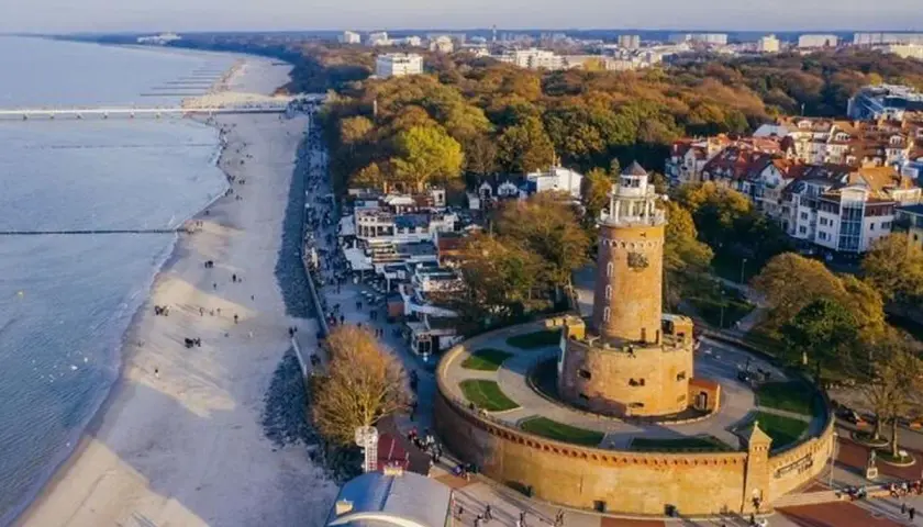 Widok na latarnie morskie w Polsce, z charakterystyczną wieżą w Kołobrzegu, plażą i morzem.
