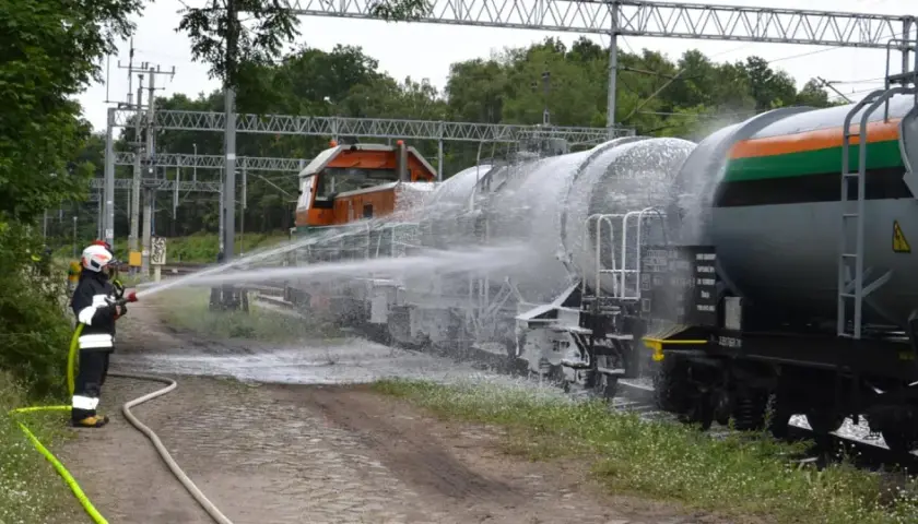 Strażak w akcji kolejowe ratownictwo techniczne. Piana gaśnicza spływa po cysternach kolejowych.