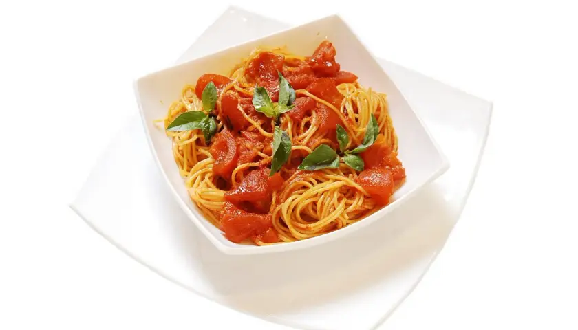 Un invitante piatto di spaghetti al pomodoro fresco, guarnito con foglie di basilico verde brillante, pronto per essere gustato.