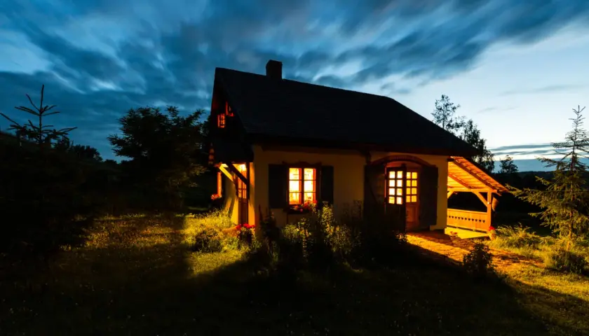 Przytulny domek na cisowym wzgórzu, oświetlony ciepłym światłem z okien, na tle rozmytego, granatowego nieba.