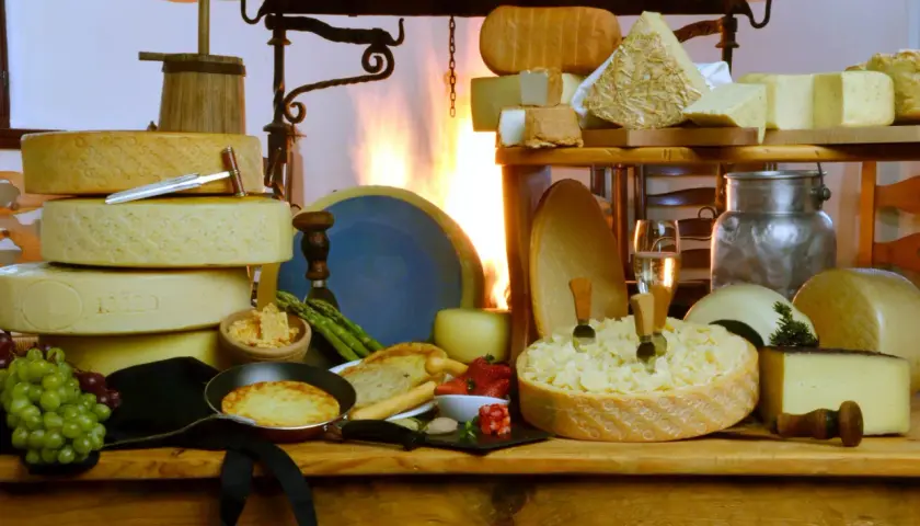 Un'abbondante tavola di formaggi, con una grande forma scavata che ricorda una fonduta di caprino, accompagnata da uva, fragole e pane tostato.