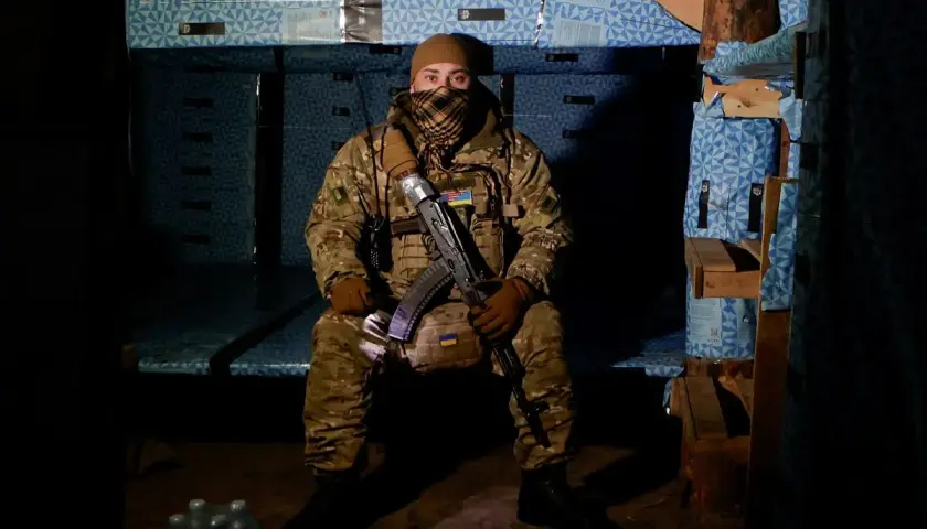 Żołnierz w mundurze, z karabinem, w ukryciu. Widać ukraińskie flagi, symbolizujące jego stopnie wojskowe Ukraina.