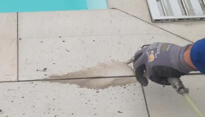 Arbeiter erneuert mit Sprühpistole die Silikonfugen auf gefliestem Boden neben einem Pool.