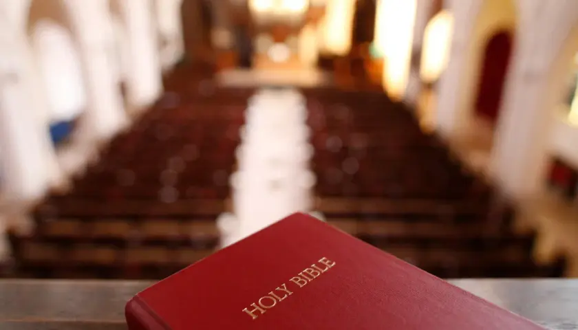 Czerwona Biblia leży na pierwszym planie, w tle widać rzędy pustych ławek w kościele, gdzie gromadzą się protestanci.