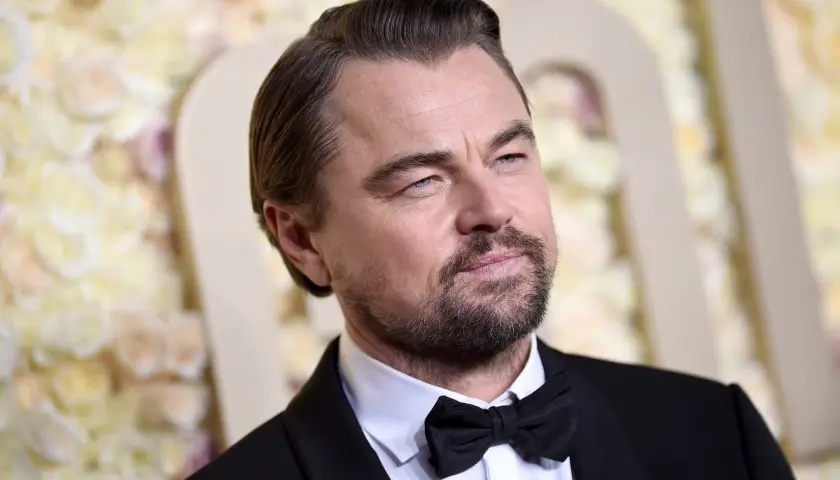 Leonardo DiCaprio wiek: doświadczony aktor w czarnym smokingu z muszką, z siwiejącymi włosami i kilkudniowym zarostem.
