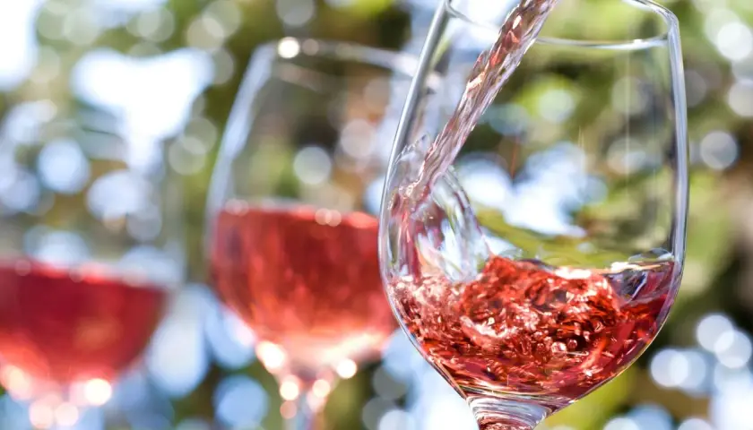Vin rosé versé dans un verre, avec d'autres verres en arrière-plan flou.