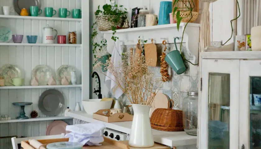 A cozy granny chic kitchen with shelves full of colorful mugs, plates, and jars. A bouquet of dried flowers adds a rustic touch.