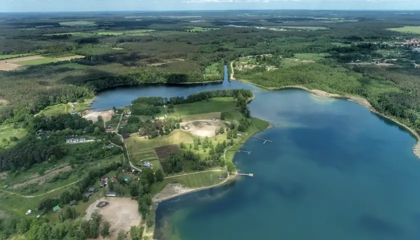 Malownicze jezioro Niesłysz otoczone lasami, z widocznymi domkami letniskowymi i pomostami.