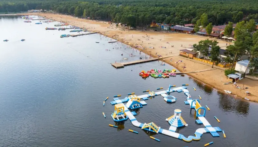 Sielpia atrakcje: dmuchany plac zabaw na wodzie, plaża z ludźmi, wypożyczalnia sprzętu wodnego i las.