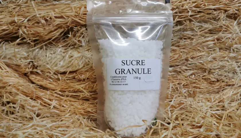 Un sachet de sucre granulé, 150g, est présenté sur un lit de copeaux de bois. Ce sucre granulé, c'est quoi ? C'est du sucre cristallisé.