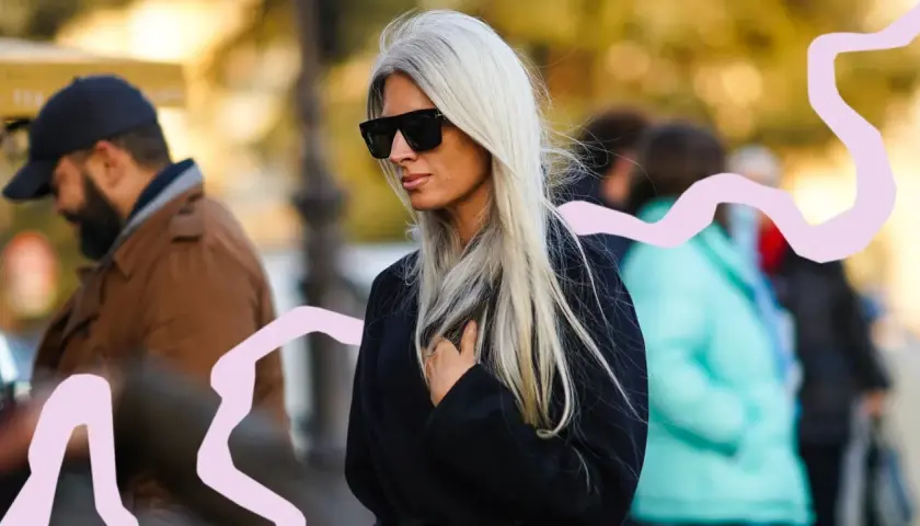 Mujer con pelo blanco largo y liso, gafas de sol oscuras y abrigo negro. La moda pelo blanco mujer es tendencia.