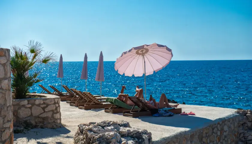 Relaks na plaży w Czarnogórze. Czy czarnogóra jest bezpieczna? Turyści odpoczywają na leżakach przy turkusowym morzu.